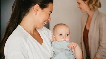 Pedagogisch Medewerker op de kinderopvang houdt baby vast en lacht naar baby